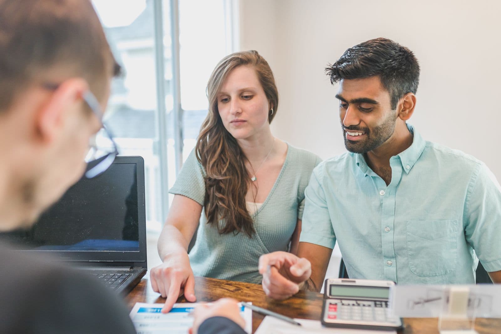 A couple going through their financial position with an adviser across a desk, documents and a calculator between them.